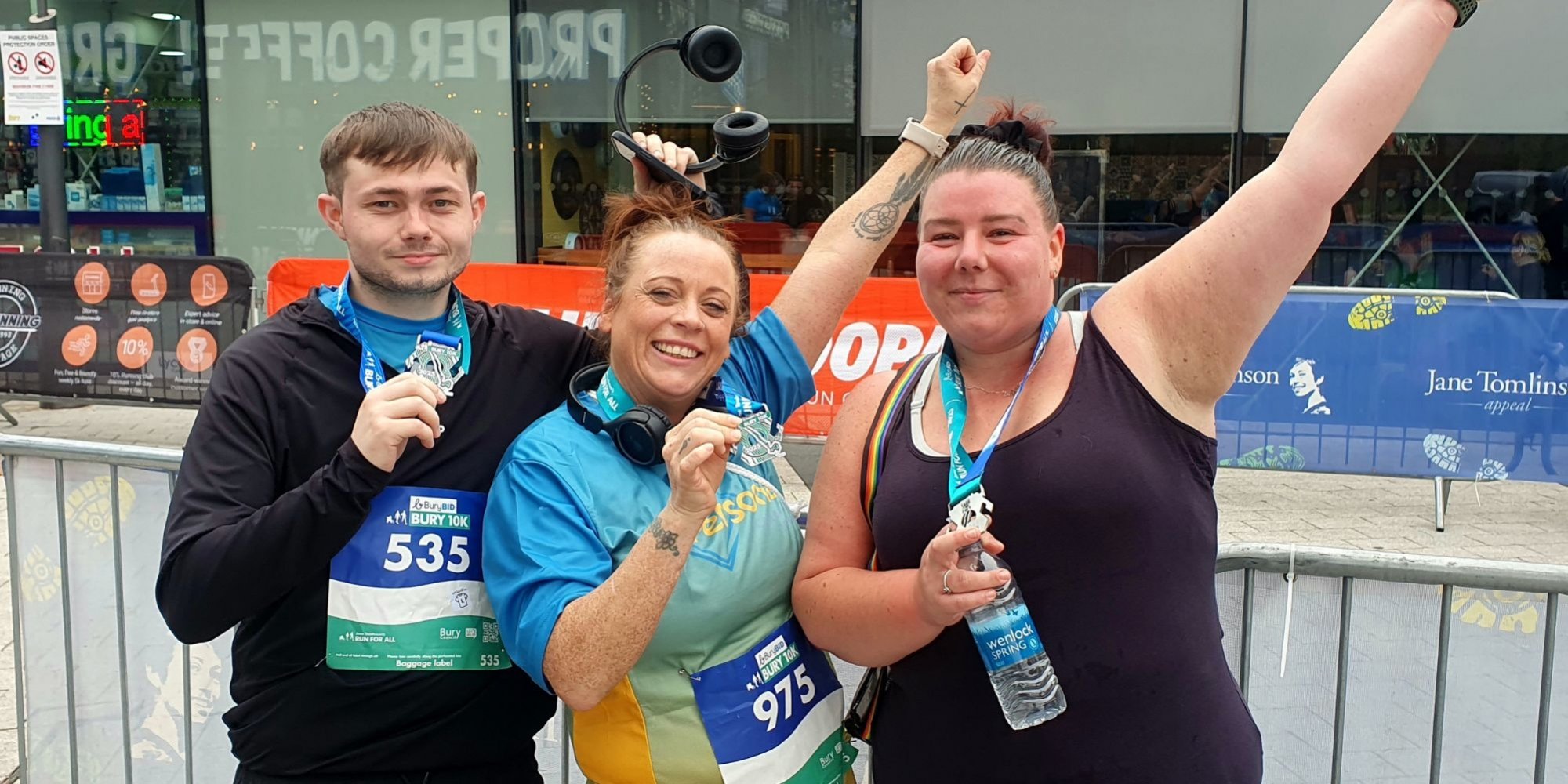 photo of 2 women and a man holding their 10k medals. The women have one arm in the air.