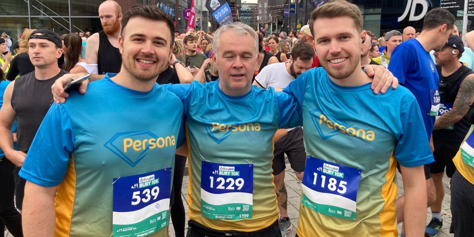 photo of 3 men with their arms round each other, smiling to camera. They are wearing matching blue tshirts.