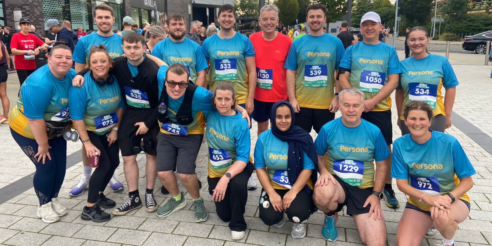 Photo of 15 men and women wearing matching running t-shirts and smiling to camera.