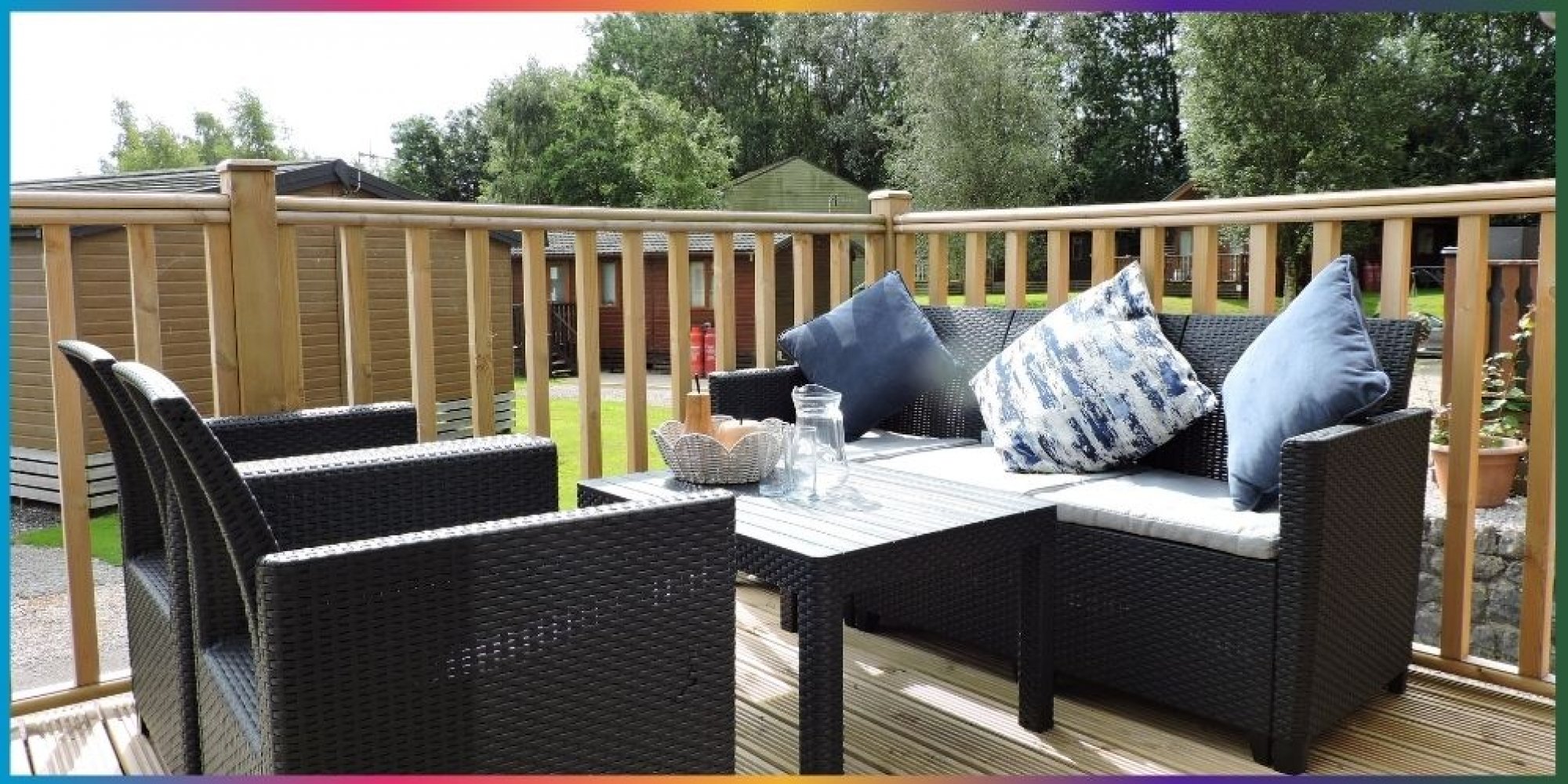 photos: decking with 2 armchairs, a sofa and coffee table. Blue and white cushions on the sofa & a jug of juice on the table