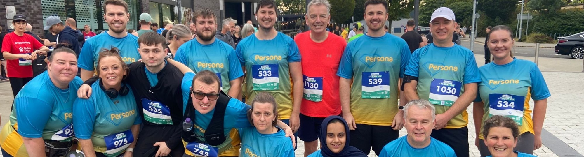 Photo of 15 men and women wearing matching running t-shirts and smiling to camera.