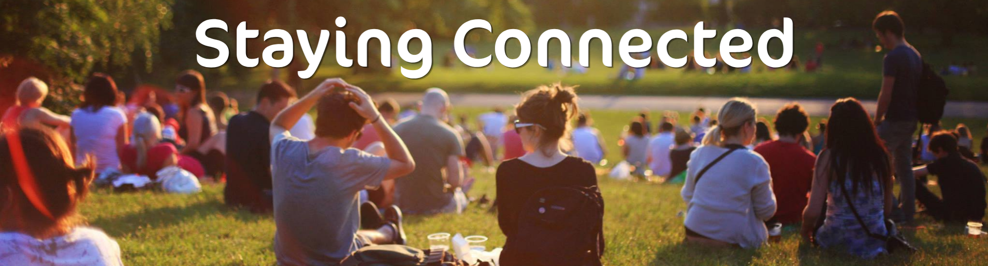 Lots of people sat on a field in the sunshine with the words 'Staying Connected' 