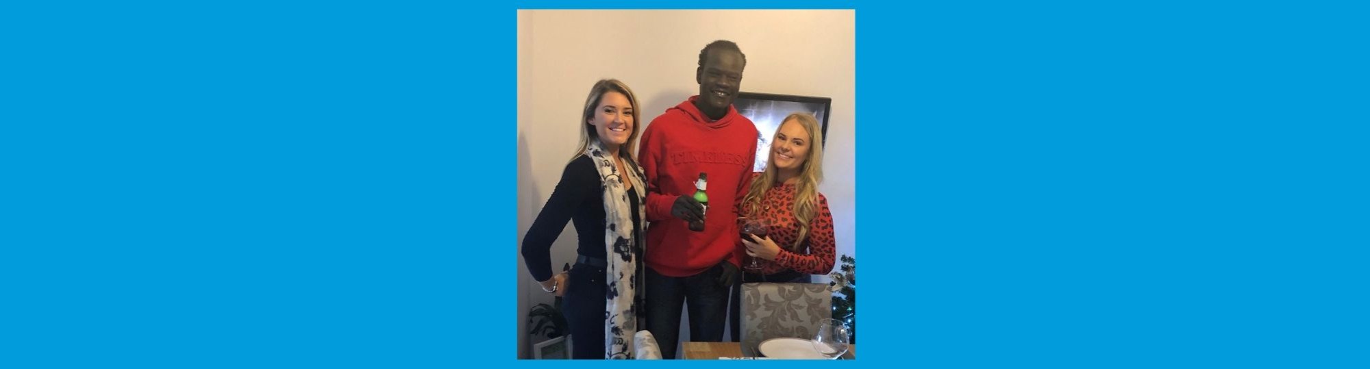 Blue background with photo of a man standing with two women. They are smiling to camera and he is holding a beer.