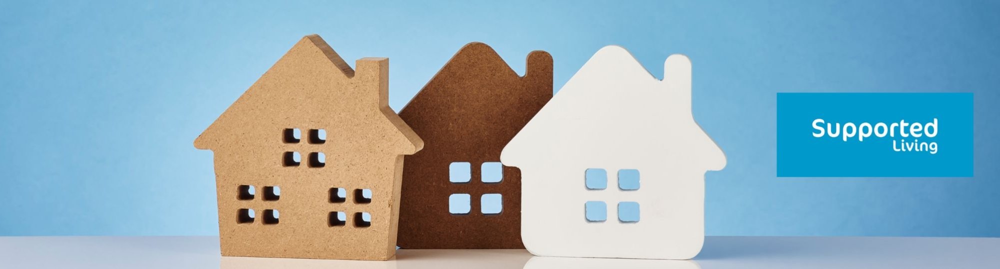 A picture of three little wooden houses with a blue background and the Supported Living logo